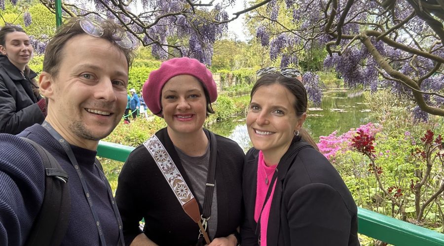 Happy travelers at Monet's Japanese bridge with wisteria blooms and water lily pond at Giverny gardens