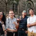 Smiling guide with three guests looking up at Paris architecture during a walking Paris city tour on a sunny day