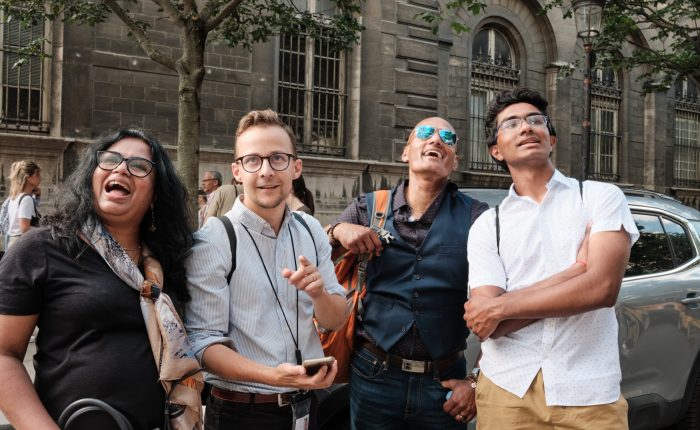 Smiling guide with three guests looking up at Paris architecture during a walking Paris city tour on a sunny day