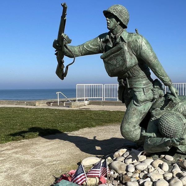 Bronze statue of two American soldiers advancing across Omaha Beach, overlooking the sea with small U.S. flags at the base.