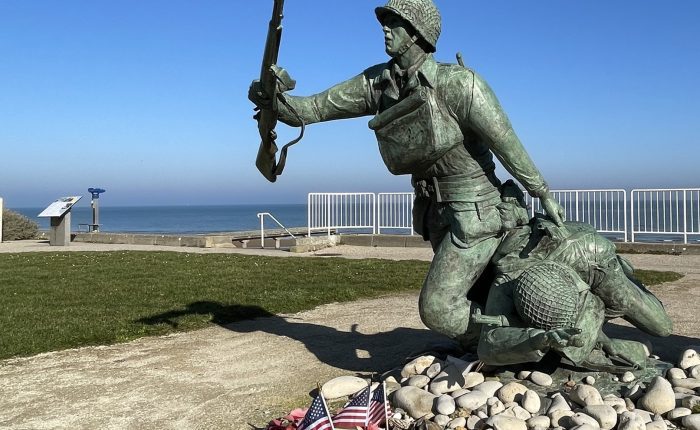 Bronze statue of two American soldiers advancing across Omaha Beach, overlooking the sea with small U.S. flags at the base.