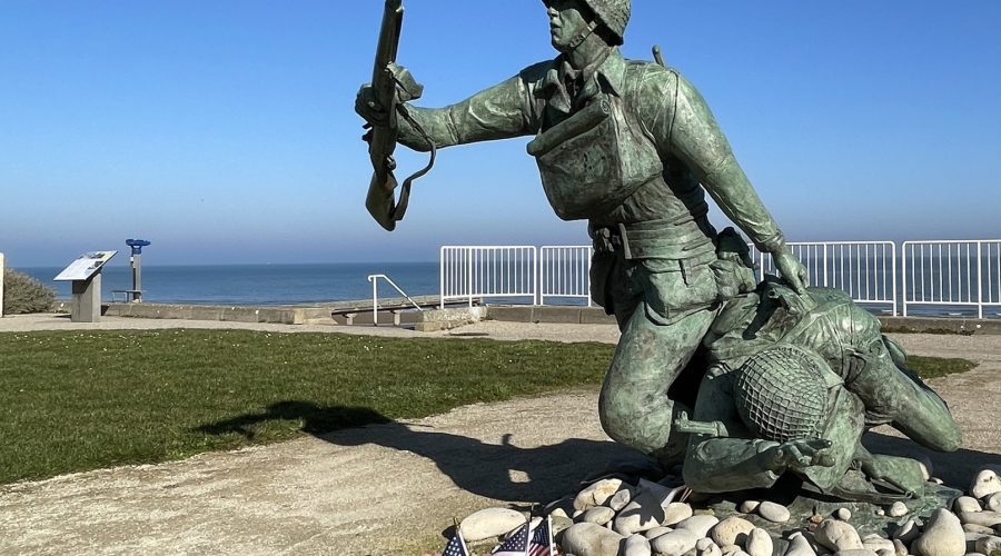Bronze statue of two American soldiers advancing across Omaha Beach, overlooking the sea with small U.S. flags at the base.