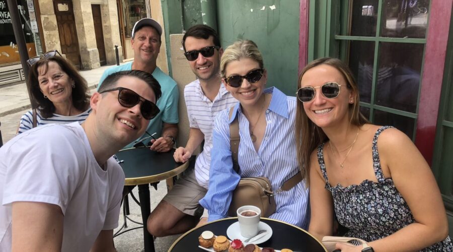 Group of friends and relatives seated at a Paris café table enjoying pastries and coffee during a city tour stop.