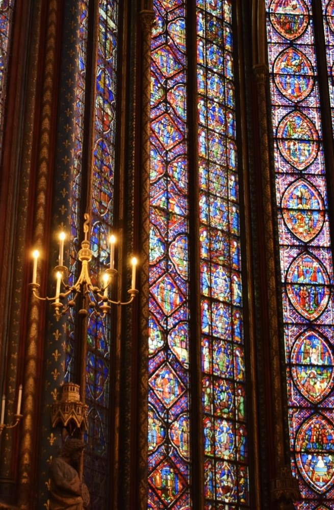 Golden chandelier and richly detailed stained-glass windows fill the upper chapel of Sainte-Chapelle with colorful light during a private tour