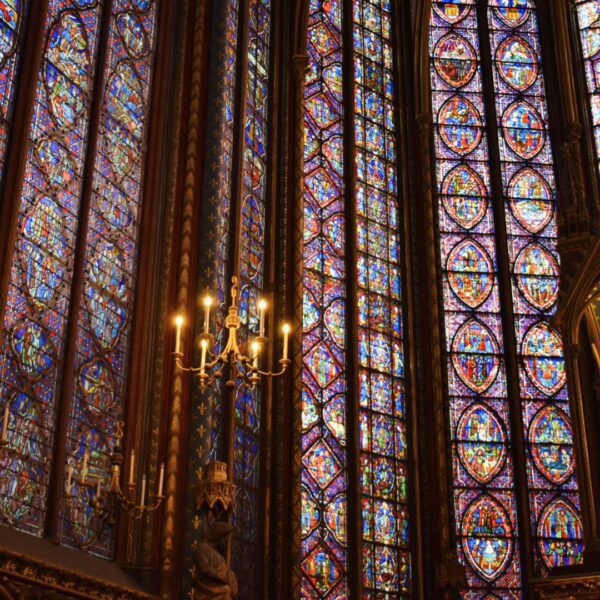Golden chandelier and richly detailed stained-glass windows fill the upper chapel of Sainte-Chapelle with colorful light during a private tour