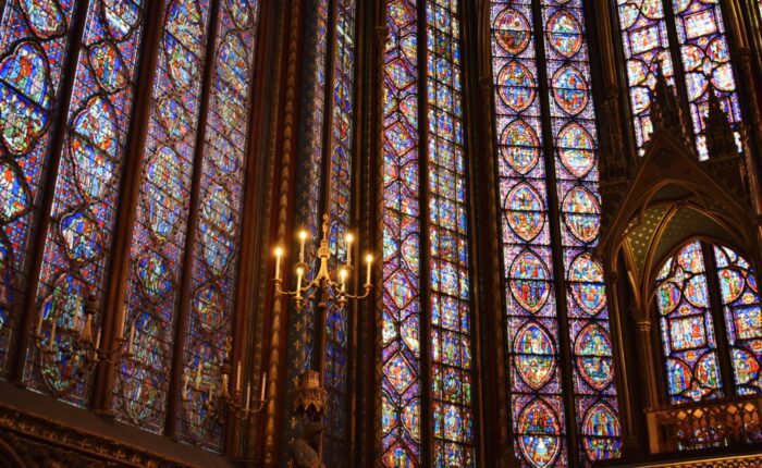 Golden chandelier and richly detailed stained-glass windows fill the upper chapel of Sainte-Chapelle with colorful light during a private tour