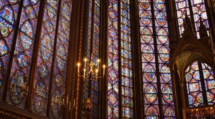 Golden chandelier and richly detailed stained-glass windows fill the upper chapel of Sainte-Chapelle with colorful light during a private tour