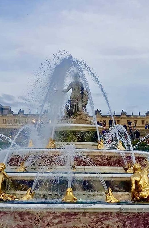 Grand fountain in the Versailles gardens spraying water with the palace in the background during a private full day tour.