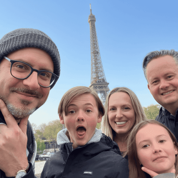 Smiling family and their guide taking a selfie in front of the Eiffel Tower during a private Paris city tour.