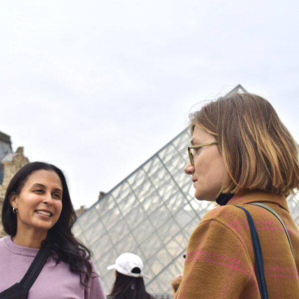 Two women chat with their guide outside the Louvre, with the glass pyramid rising behind them