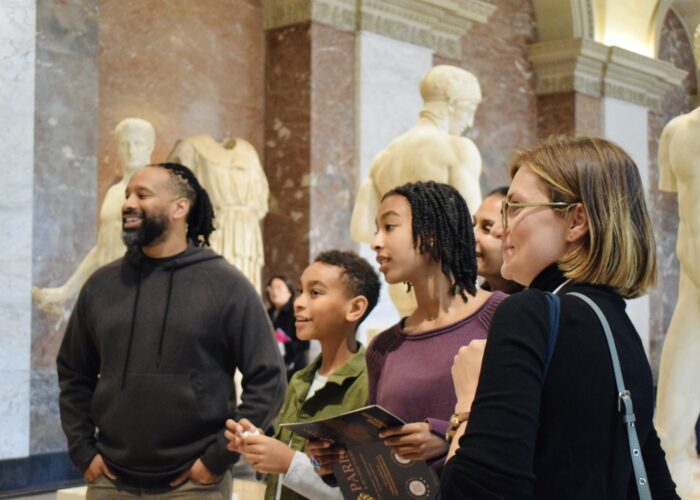 Family with Paris and Beyond Tours guide exploring classical sculptures during interactive Louvre Museum scavenger hunt