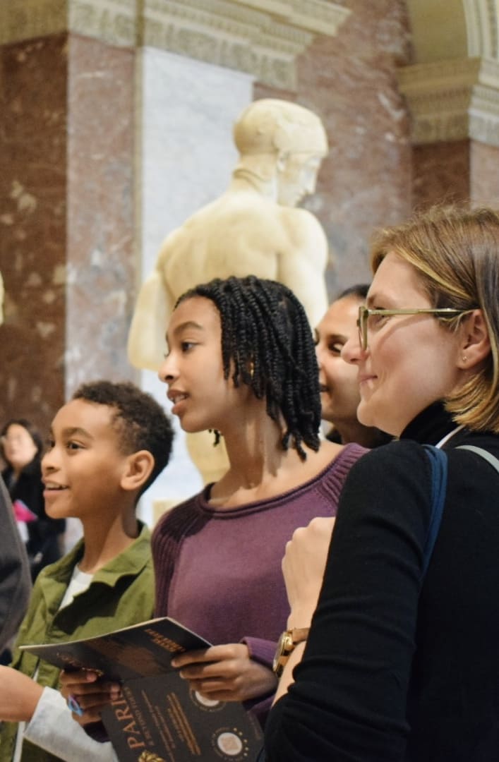 Kotryna guiding children during Louvre treasure hunt tour with Paris and Beyond Tours, kids exploring ancient sculptures