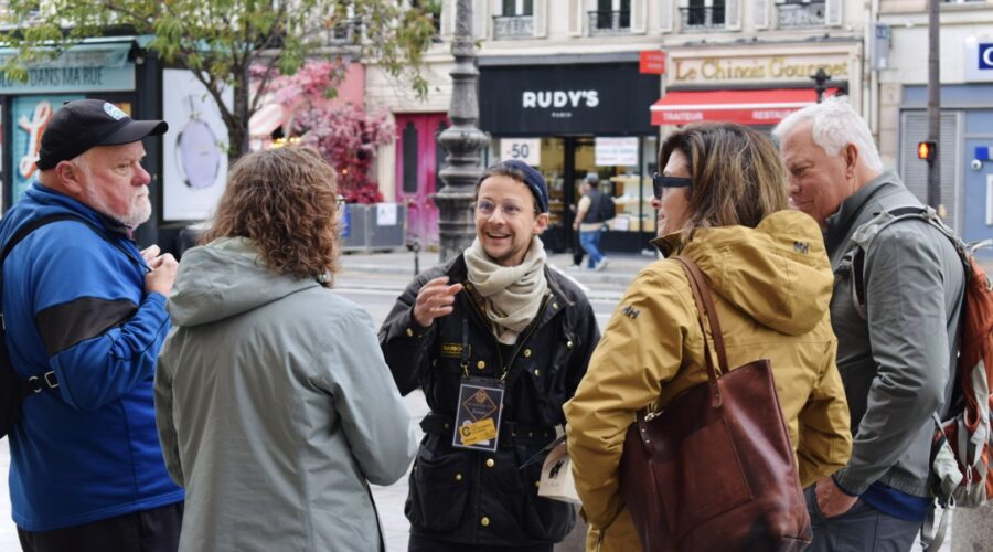 Guide chatting and smiling with a small group of guests on a busy Marais street during a private Paris food tour