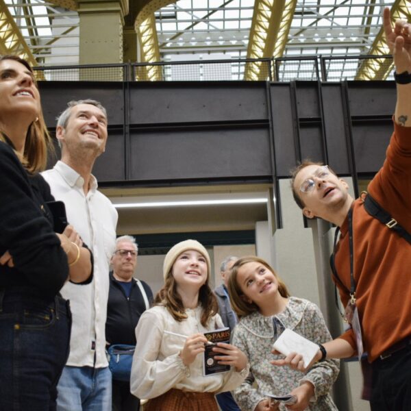 Family and guide stand in Orsay’s main hall, smiling and looking up as they follow the next treasure hunt clue on a private tour for kids.