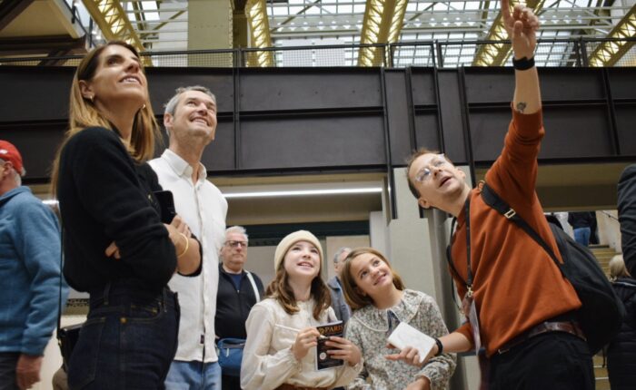 Family and guide stand in Orsay’s main hall, smiling and looking up as they follow the next treasure hunt clue on a private tour for kids.