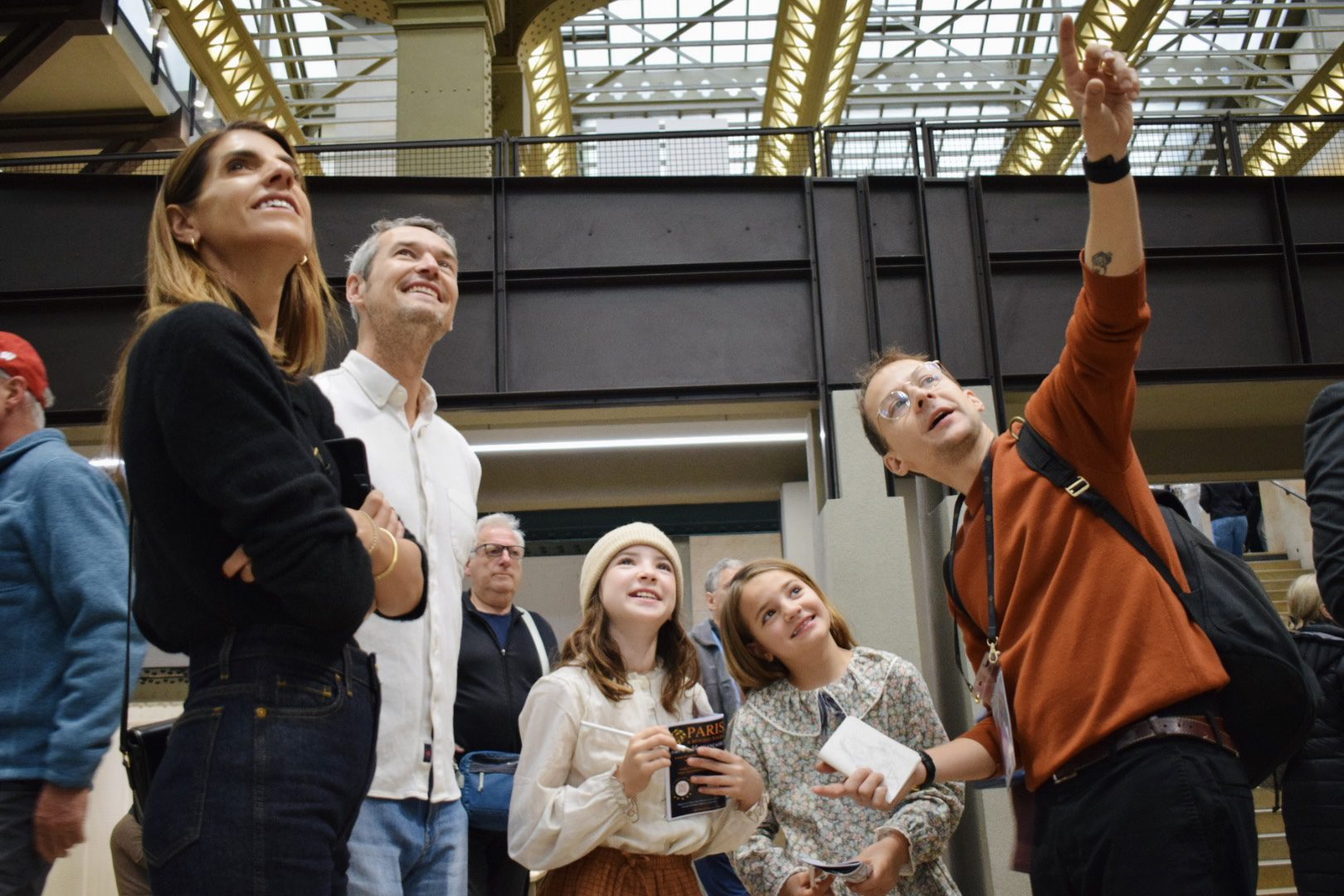 Family and guide stand in Orsay’s main hall, smiling and looking up as they follow the next treasure hunt clue on a private tour for kids.