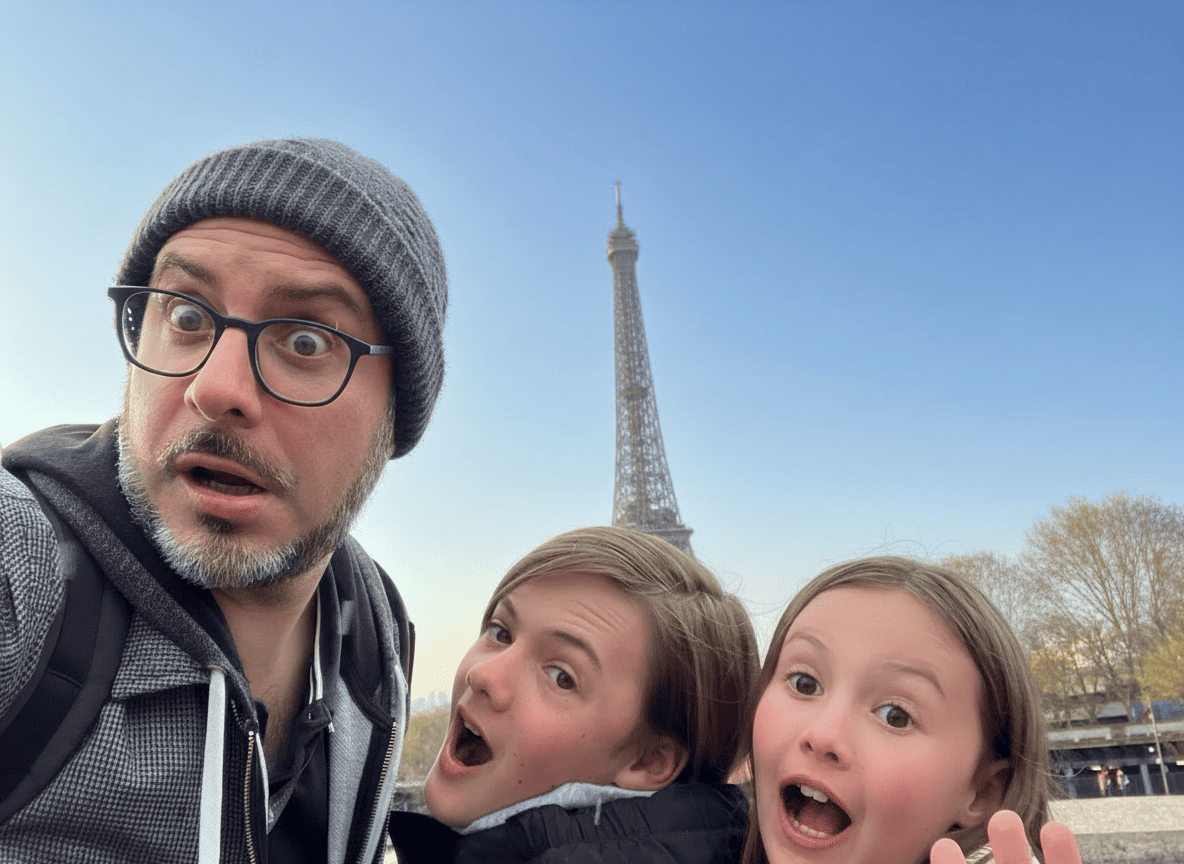 Playful Guide and two children pulling surprised faces with the Eiffel Tower behind them on a family Paris highlights tour.