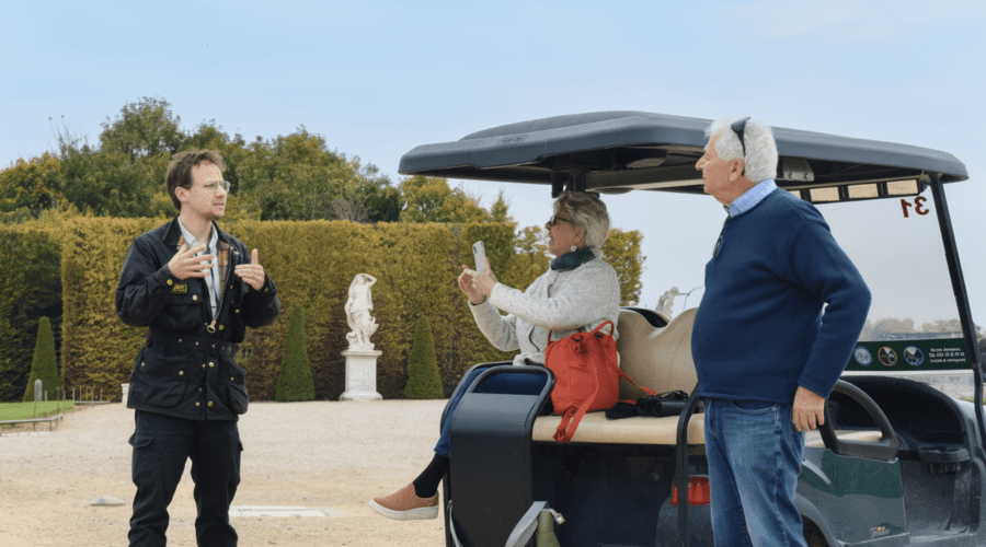 Guide explaining Versailles gardens history to an older couple seated on a golf cart during a relaxed private Versailles tour.