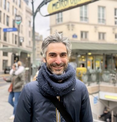 Tour guide Ed smiling at camera in front of Métropolitain Paris Metro sign wearing navy scarf and jacket