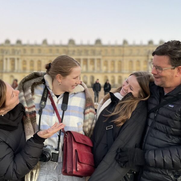 Family of four standing together smiling in the courtyard of the Palace of Versailles with the grand golden facade of the palace in the background