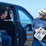 Paris and Beyond Tours guide showing 1944 D-Day historical photos to guest at Normandy landing beach private luxury minivan tour from Bayeux Caen