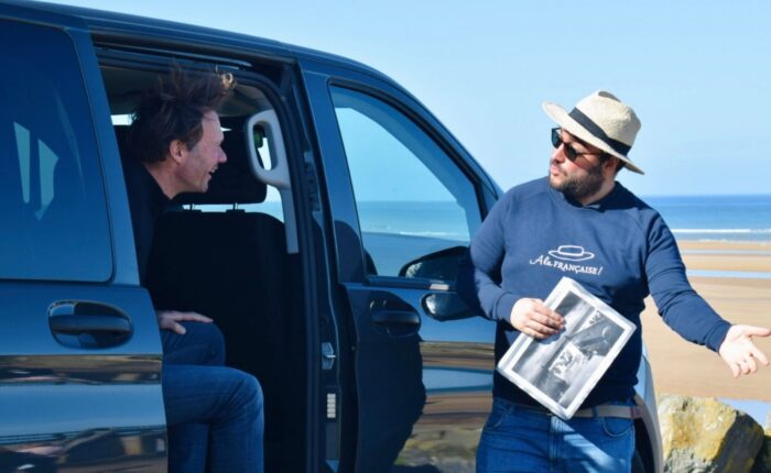 Paris and Beyond Tours guide showing 1944 D-Day historical photos to guest at Normandy landing beach private luxury minivan tour from Bayeux Caen